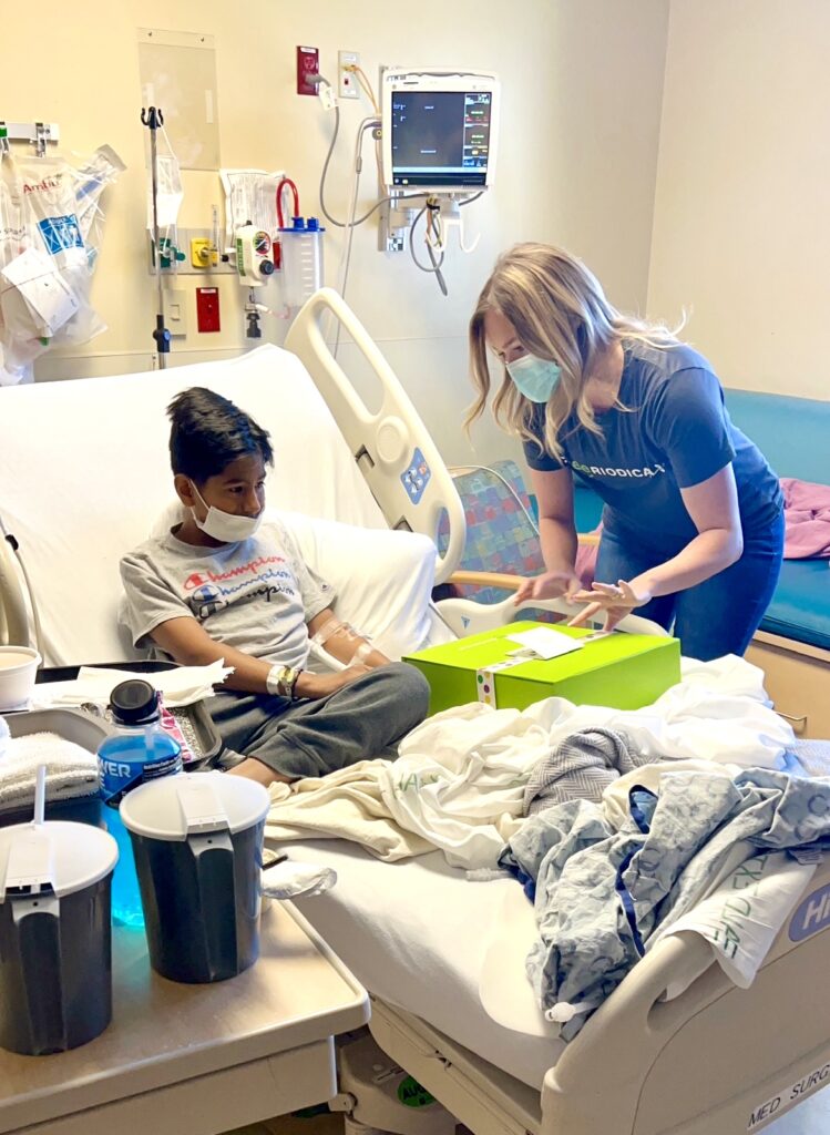 Cheeriodicals employees helps a little boy in a hospital bed open a bright green Cheeriodicals box of toys