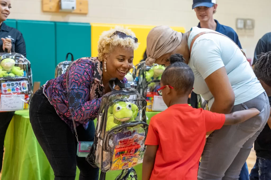 Sonic Automotive woman hands a young boy a Cheeriodicals backpack full of school supplies