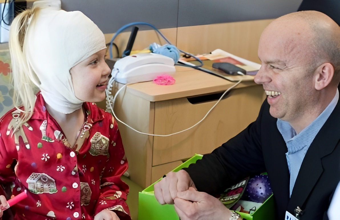 A man smiles with a little girl in a head wrap in the hospital
