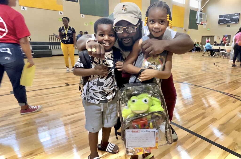 A father smiles with his two kids and their new Cheeriodicals backpacks filled with new school supplies